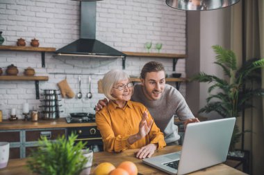 Gri gömlekli genç yakışıklı adam ve annesi mutlu görünüyor.