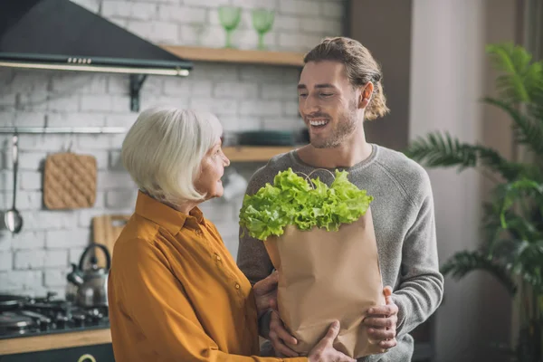 Mladý muž s balíčkem zelených usmívá se na svou matku — Stock fotografie