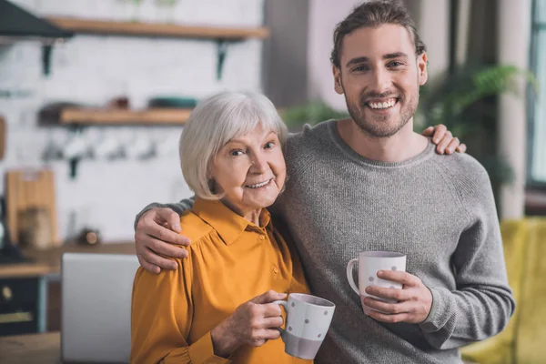 Joven hombre guapo en camisa gris y su madre sintiéndose increíble juntos — Foto de Stock