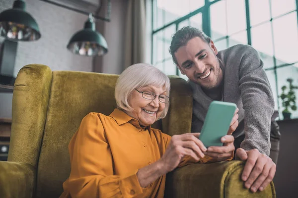Starsza pani w żółtym uczy się korzystania ze smartfona — Zdjęcie stockowe