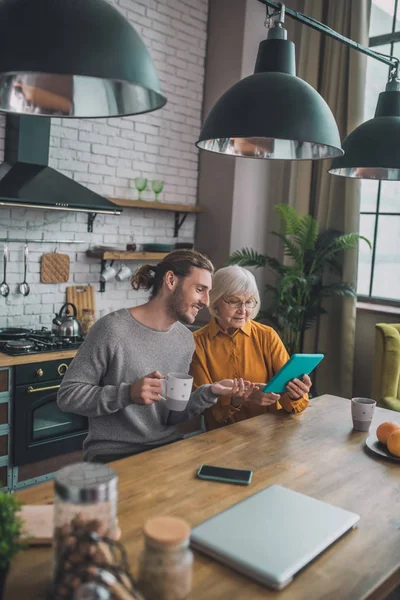 Jovem homem bonito em camisa cinza e sua mãe olhando para o tablet — Fotografia de Stock