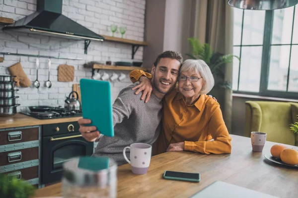 Joven hombre guapo en camisa gris y su mamá haciendo selfie — Foto de Stock