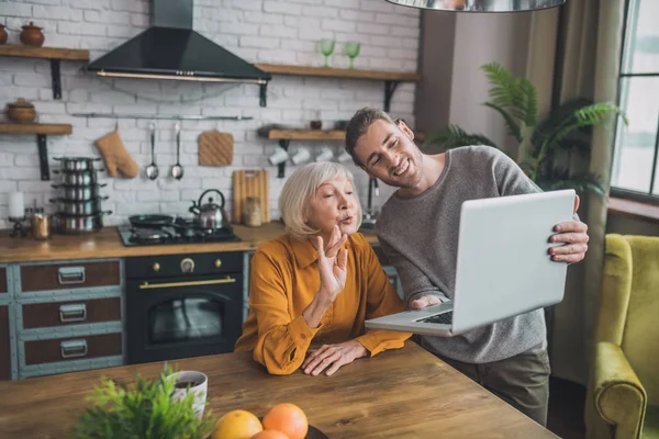 Joven hombre guapo en camisa gris y su mamá teniendo videollamada con amigos — Foto de Stock