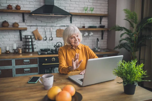 Bien parecido anciana en amarillo teniendo una videollamada — Foto de Stock