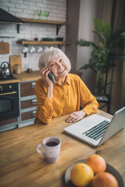 Vakker, eldre dame i gult som snakker i telefonen – stockfoto