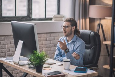 Mavi tişörtlü genç adam video konferansı yapıyor.