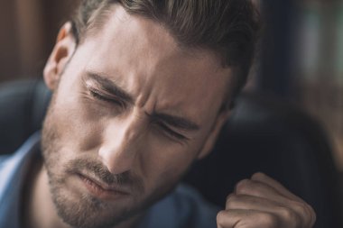 Mavi gömlekli genç sakallı adam baş ağrısı çekiyor.