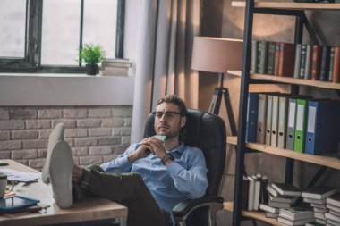 Gözlüklü, işten sonra dinlenen genç, sakallı bir ofis çalışanı.