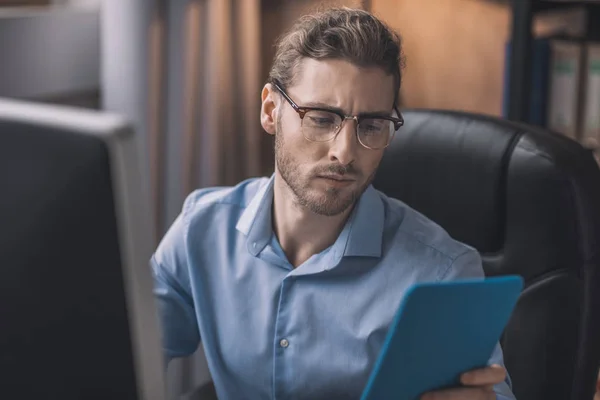 Ung skäggig man i blå skjorta håller tablett i händerna — Stockfoto