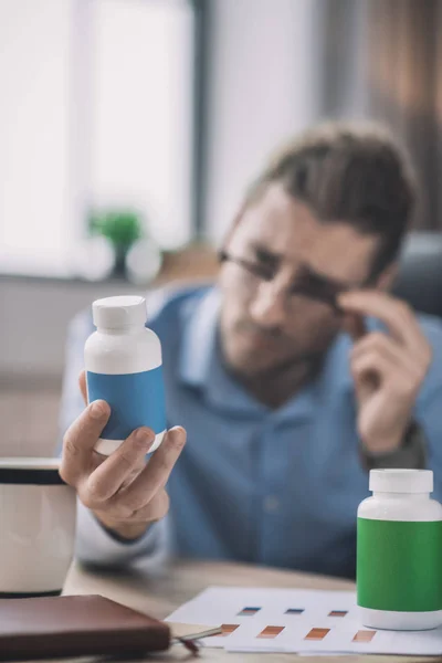 Homem barbudo de camisa azul olhando para o botle com pílulas — Fotografia de Stock