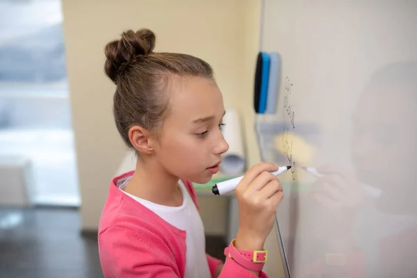 Geconcentreerd meisje dat op het whiteboard schrijft in de klas — Stockfoto