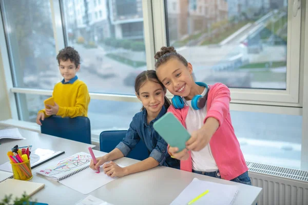 Duas meninas fazendo selfie na escola usando um smartphone — Fotografia de Stock