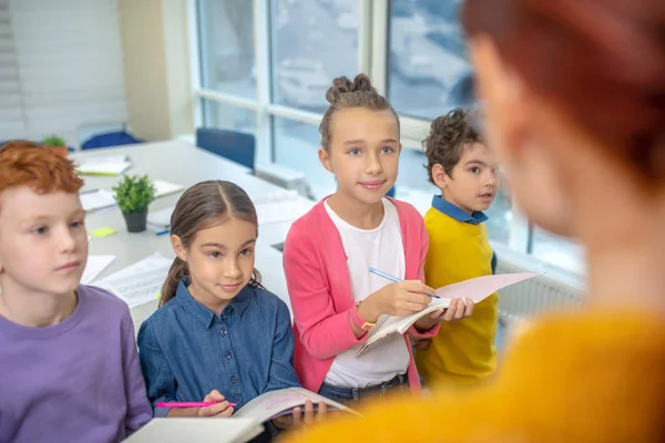 A gyerekek hallgatják a tanárt és jegyzetelnek. — Stock Fotó