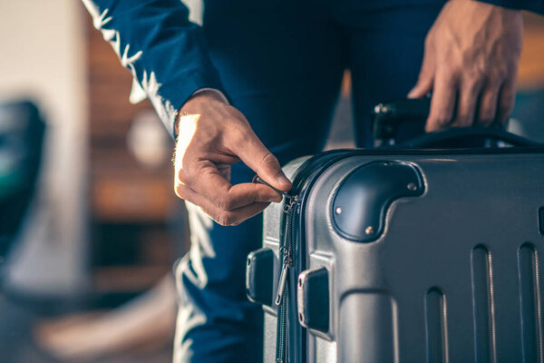 Close up picture of a man zipping his suitcase