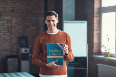 İngilizce dil bilgisi kitabı tutarken gülümseyen yakışıklı öğrenci