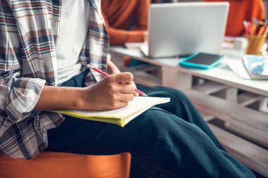 İşaretli gömlek giyen öğrenci kalem tutuyor ve yazıyor.