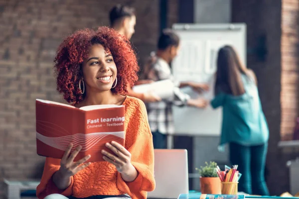 Estudiante alegre vistiendo suéter naranja leyendo libro chino —  Fotos de Stock