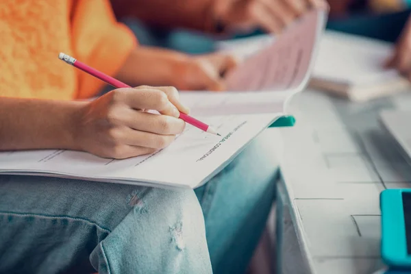 Close up of student wearing jeans holding pencil while making notes — Stock Photo, Image