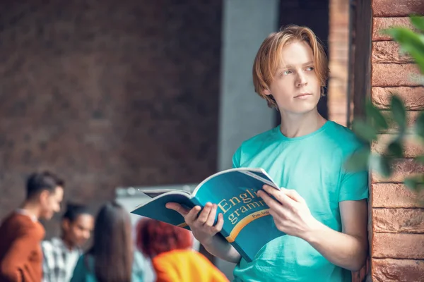 Studente in piedi vicino muro di mattoni e la lettura di grammatica inglese libro — Foto Stock