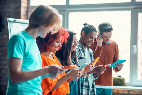 Fröhliche Studenten, die ihre Geräte benutzen, während sie wenig Pause haben — Stockfoto