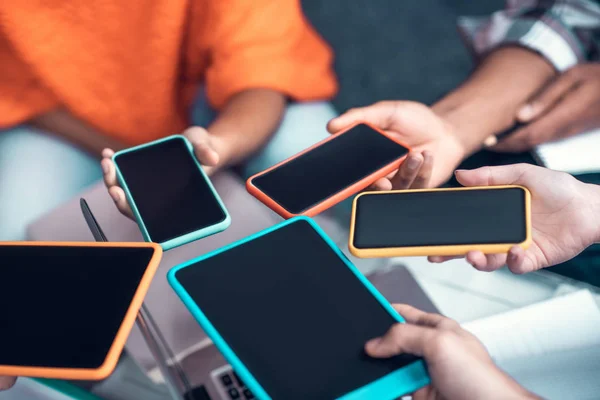 Estudantes segurando smartphones e tablets enquanto usam dispositivos — Fotografia de Stock