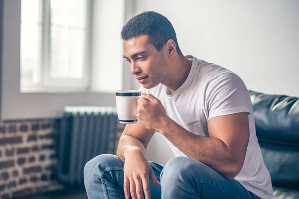 Guy thinking in a chair with a cup in his hand.