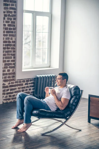 Νεαρός αθλητικός τύπος σε μια καρέκλα πίνοντας καφέ. — Φωτογραφία Αρχείου