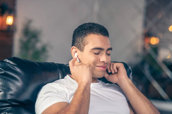 Joven chico descansando escuchando música con auriculares inalámbricos . — Foto de Stock
