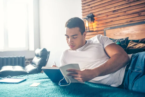 Mann schreibt Übungen in ein Notizbuch, während er auf einem Bett liegt. — Stockfoto