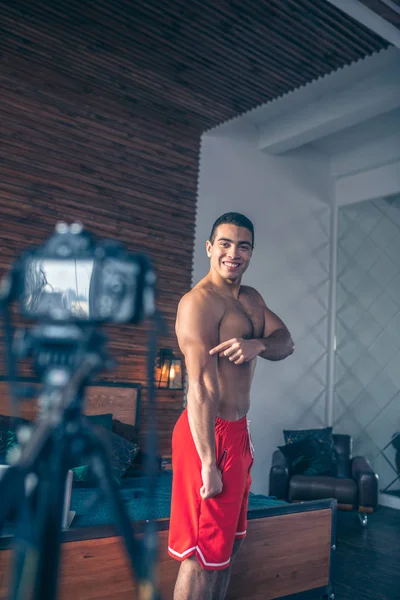 Joven vlogger deportivo en pantalones cortos rojos mostrando sus tríceps —  Fotos de Stock