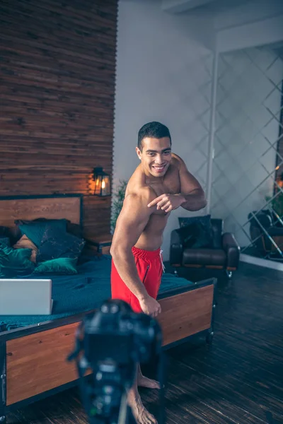 Joven vlogger deportivo en pantalones cortos rojos demostrando sus fuertes músculos —  Fotos de Stock