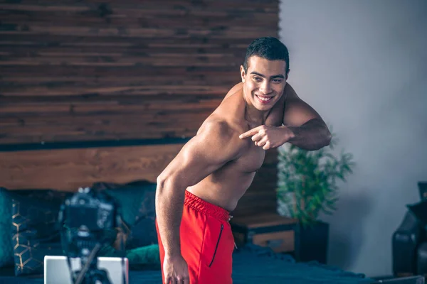 Joven vlogger deportivo en pantalones cortos rojos demostrando sus bíceps — Foto de Stock