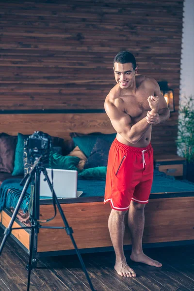 Giovane vlogger sportivo fit in pantaloncini rossi che dimostra le sue braccia forti — Foto Stock
