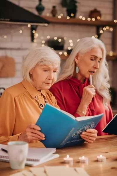 Dos señoras lindas agradables de pelo gris que parecen involucradas mientras estudian juntas — Foto de Stock