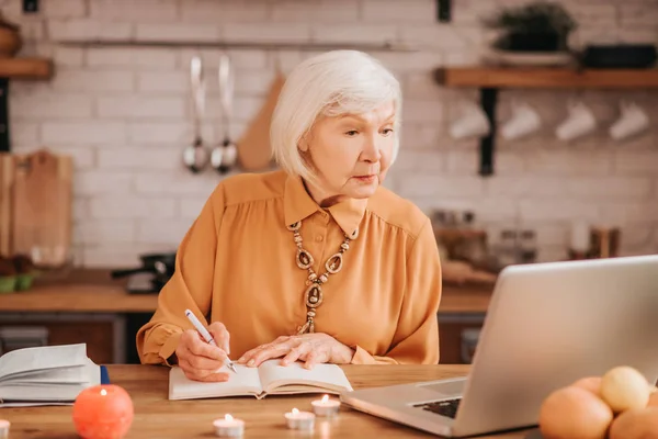 Mujer de pelo gris hermosa anciana en blusa naranja leyendo una lección en línea — Foto de Stock