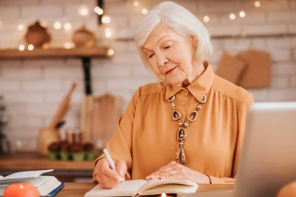 Mujer de pelo gris hermosa anciana en blusa naranja haciendo notas — Foto de Stock