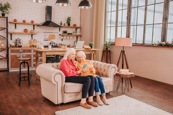 Two pleasant-looking elderly grey-haired women sitting on the sofa — Stock Photo, Image