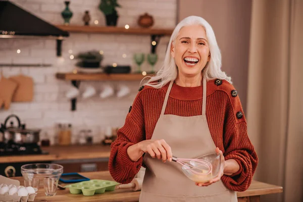 Capelli grigi signora sorridente sorridente latte montante luminoso in una ciotola — Foto Stock