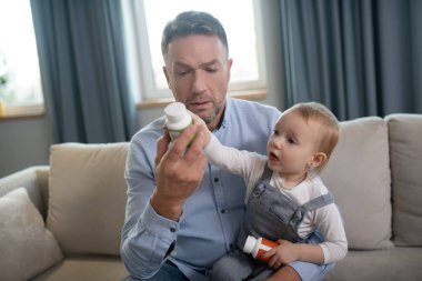 Babası çocuğunu kucağında tutuyor ve haplara ders veriyor.