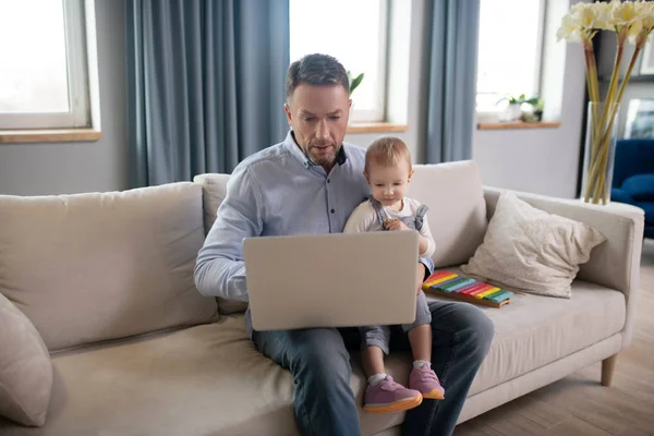 Dojrzały ojciec pracuje nad laptopem i wygląda na skoncentrowanego — Zdjęcie stockowe