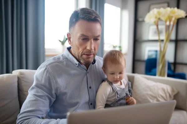 Älterer Vater hält sein Kind und arbeitet an seinem Laptop — Stockfoto