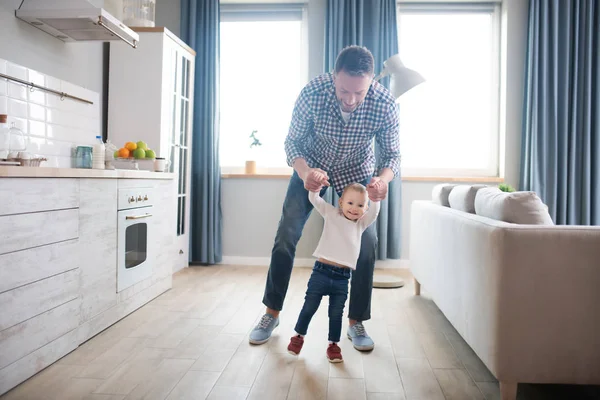 Pequeña niña linda haciendo sus primeros pasos con los papás ayudan —  Fotos de Stock