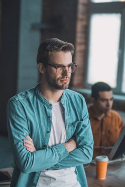 Elleri çapraz duran ciddi bir genç adam.