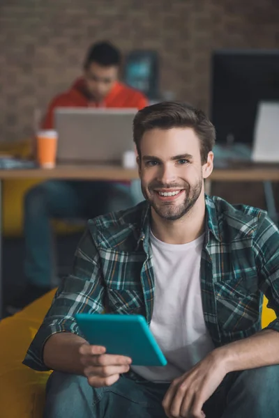 Vrolijke man met baard zittend met de tablet in zijn hand — Stockfoto