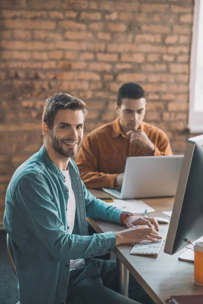 Alegre hombre inteligente sentado frente a su computadora — Foto de Stock