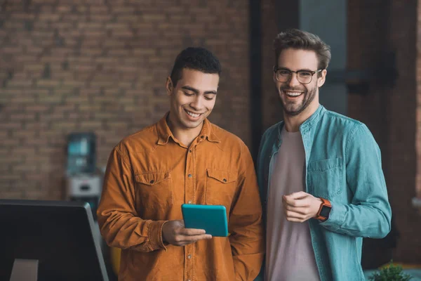 Hombres alegres y agradables de pie junto con una tableta — Foto de Stock