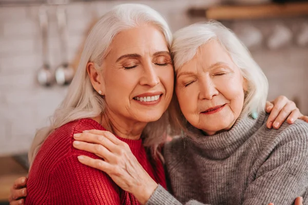 Две зрелые седовласые позитивные дамы обнимают друг друга — стоковое фото