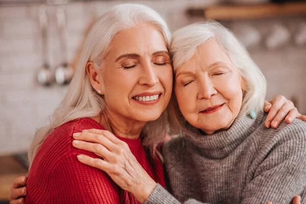 Two mature grey-haired positive ladies hugging each other