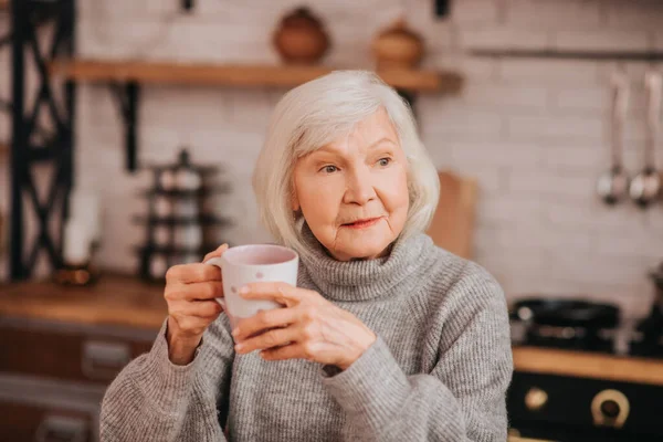 Beautiful elderly woman in grey sweater looking thoughtful — 스톡 사진