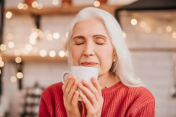 Gyönyörű idős nő piros blúzban érzi a tea illatát. — Stock Fotó